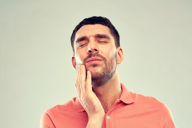 pessoas, cuidados de saúde, odontologia e conceito de problema - homem infeliz que sofre de dor de dente sobre fundo cinza