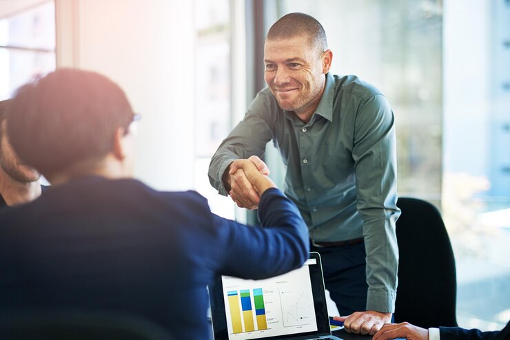 Foto pessoas da sala de reuniões e felizes em aperto de mão com estatísticas no laptop para fusão de parceria e colaboração empregados de negócios e sorriso no escritório para acordo de negócio ou trabalho em equipe para o crescimento da empresa