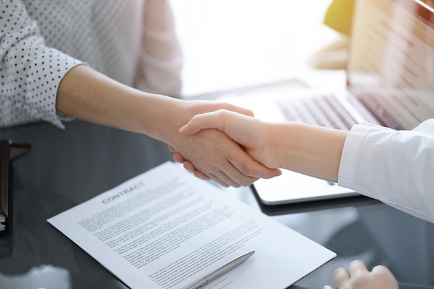 Pessoas de negócios apertando as mãos acima de papéis de contrato acabados de assinar na mesa branca, close-up. Advogados em reunião. Trabalho em equipe, parceria, conceito de sucesso.