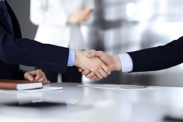 Pessoas de negócios apertando as mãos na reunião ou negociação, close-up. Grupo de empresários desconhecidos e uma mulher no fundo em um escritório moderno. Conceito de trabalho em equipe, parceria e aperto de mão.