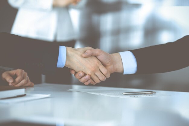 Pessoas de negócios apertando as mãos na reunião ou negociação, close-up. Grupo de empresários desconhecidos e uma mulher no fundo em um escritório moderno. Conceito de trabalho em equipe, parceria e aperto de mão.