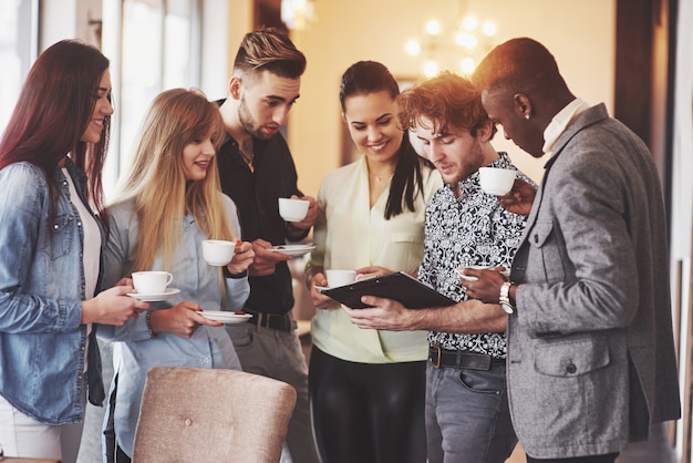 Pessoas de negócios bem sucedidos estão usando gadgets, conversando e sorrindo durante a pausa para o café no escritório