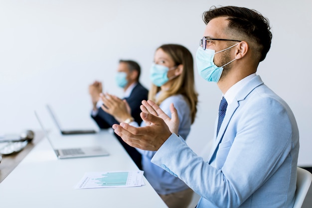 Pessoas de negócios com máscaras de proteção batendo palmas após uma reunião de negócios bem sucedido no escritório moderno