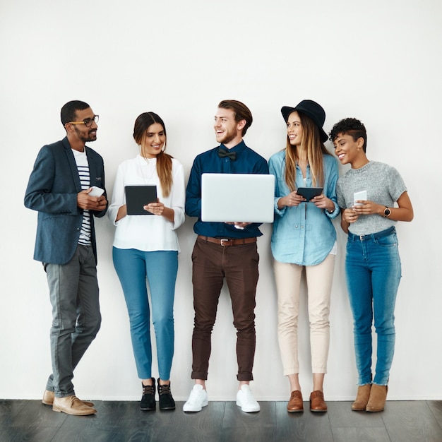 Pessoas de negócios sala de espera e colaboração com tecnologia em fila em um fundo de parede Grupo jovem ou funcionários com sorriso em laptop tablet ou telefone para pesquisa de emprego ou oportunidade de carreira