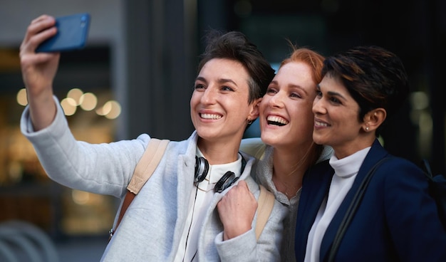 Pessoas de negócios sorriem e mulheres tiram selfie na cidade para uma memória feliz na cidade ao ar livre Foto de perfil do fotógrafo e grupo de amigos ou colegas de trabalho rindo e tirando fotos para a mídia social