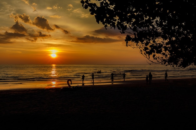 Pessoas de silhueta na praia do sol com céu laranja com lindo azul