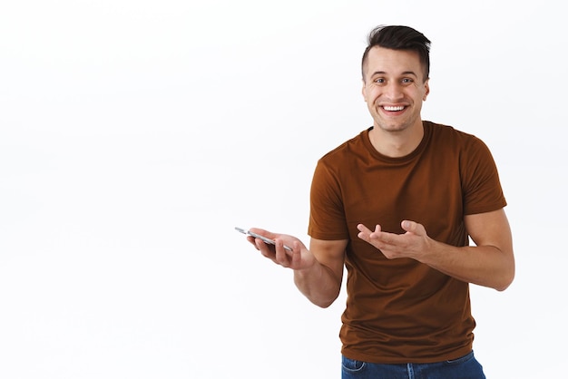 Pessoas de tecnologia e conceito de comunicação Cara feliz rindo em camiseta marrom sorrindo com sorriso satisfeito segurando o celular apontando para o smartphone tão impressionado com o novo aplicativo incrível