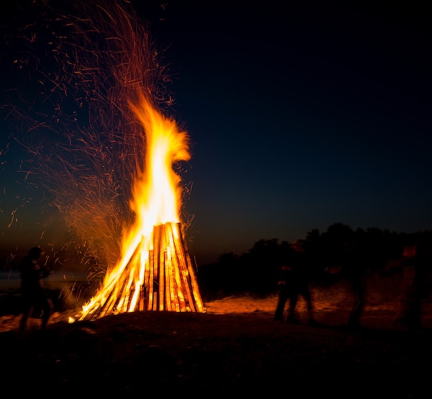 Pessoas descansando perto de uma grande fogueira ao ar livre à noite