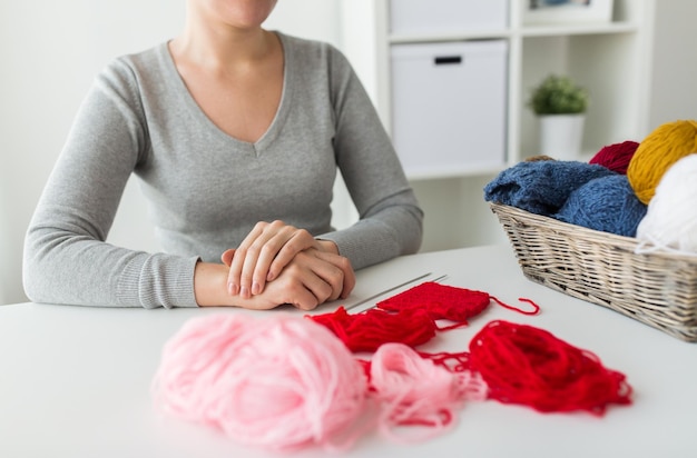 pessoas e conceito de bordado - mulher sentada à mesa com agulhas de tricô e bolas de fios na cesta em casa