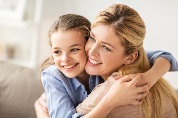 pessoas e conceito de família feliz menina sorridente com a mãe abraçando no sofá em casa