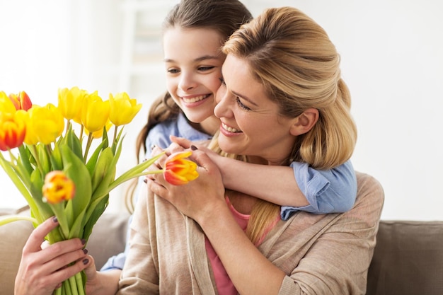 Foto pessoas e feriados conceito menina feliz dando flores de tulipas e abraçando sua mãe em casa