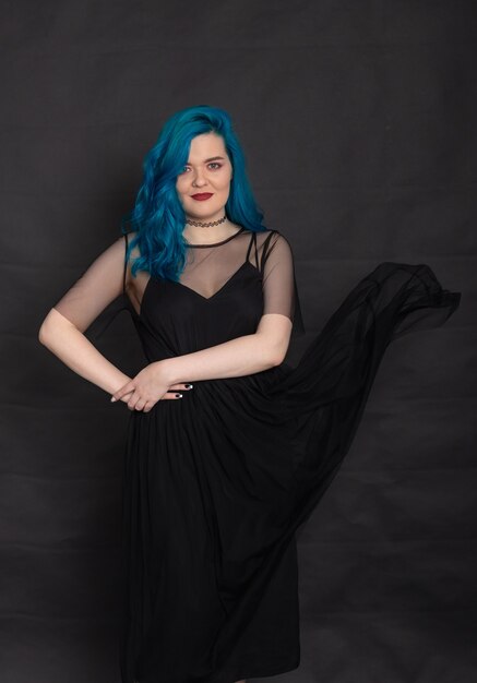 Pessoas e o conceito de moda - mulher vestida de vestido preto e cabelo azul posando sobre fundo preto.