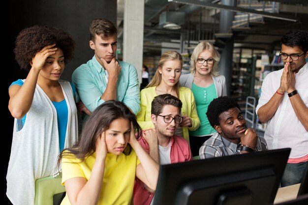 pessoas, educação, tecnologia, reprovação e conceito de escola - grupo de estudantes internacionais com computadores na biblioteca da universidade tendo algum problema