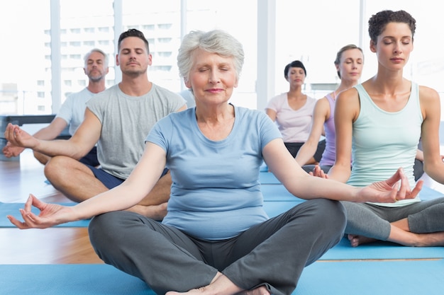 Pessoas em lotus posam com os olhos fechados no estúdio de ginástica