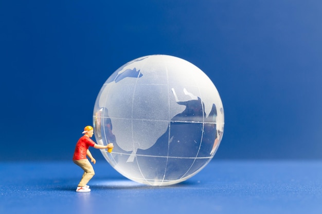 Pessoas em miniatura Adolescente pulverizando tinta globo de cristal em fundo azul Conceito do dia mundial do meio ambiente