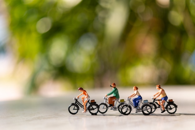 Pessoas em miniatura andam de bicicleta ao ar livre com fundo verde bokeh