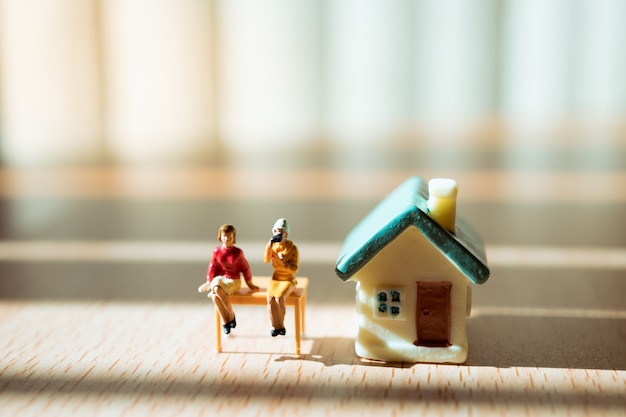 Pessoas em miniatura, casal mulher sentada na frente da casa, usando para o conceito de relação