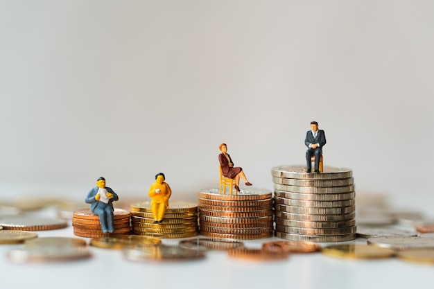 Foto pessoas em miniatura, equipe de negócios sentado na pilha moedas usando como trabalho em equipe de negócios e conceito financeiro