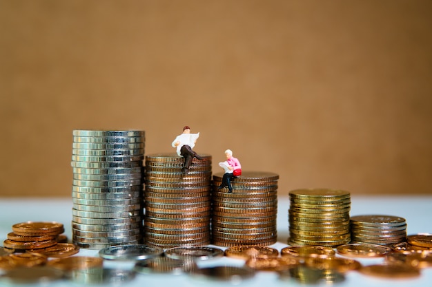 Pessoas em miniatura, homem e mulher lendo na pilha de moedas