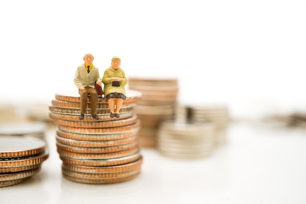 Pessoas em miniatura, idosos sentados em moedas de pilha usando como conceito de aposentadoria de emprego