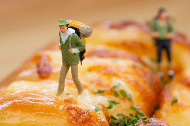 Foto pessoas em miniatura: mochileiros caminhando sobre o pão de linguiça.