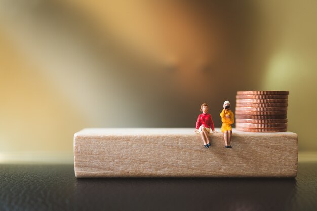 Pessoas em miniatura, mulher casal sentado no bloco de madeira com moedas de pilha usando como negócios e financ