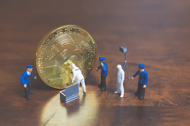 Pessoas em miniatura: polícia e detetive em pé na frente de bitcoin cryptocurrency