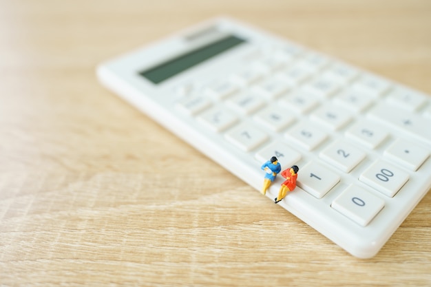 Pessoas em miniatura sentadas na calculadora branca usando como plano de fundo o conceito de negócio