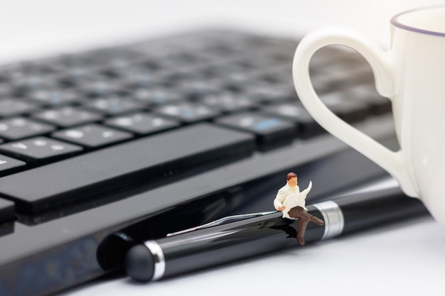 Foto pessoas em miniatura, sentado na caneta com teclado e xícara de café.