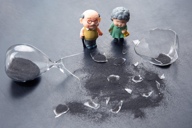 Pessoas em miniatura um casal de idosos perto de uma crise de tempo de vida de ampulheta quebrada o conceito de fim de vida para uma pessoa