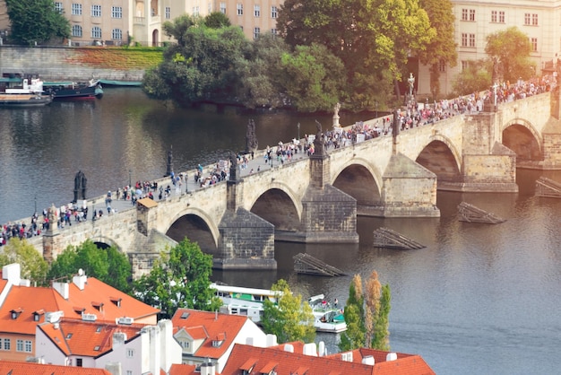 Pessoas em uma ponte de pedra sobre o rio com uma torre e esculturas em uma bela cidade velha Toned