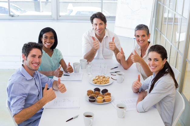 Pessoas empresárias que comem muffins dão polegares para a câmera