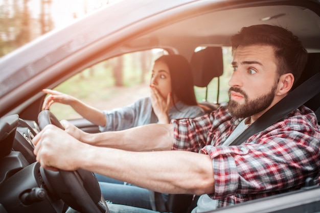 Pessoas espantadas estão sentadas no carro e olhando para a frente. Eles estão frustrados. Menina está cobrindo a boca com uma mão e apontando para a frente com outra.