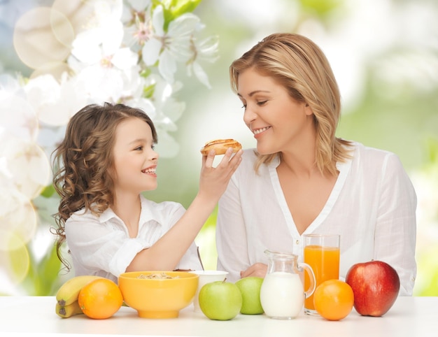 pessoas, estilo de vida saudável, família e conceito de comida - mãe e filha felizes tomando café da manhã saudável sobre fundo verde do jardim de verão