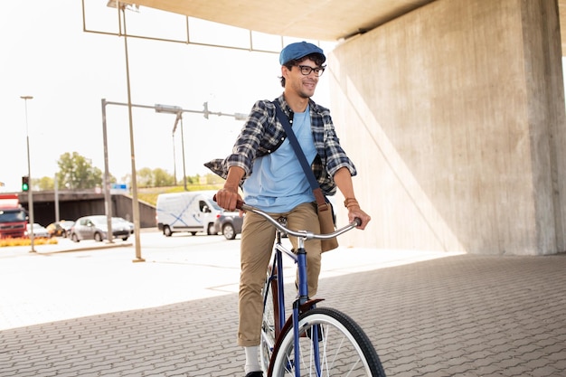 pessoas, estilo, lazer e estilo de vida - homem jovem hipster com bolsa de ombro andando de bicicleta fixa na rua da cidade