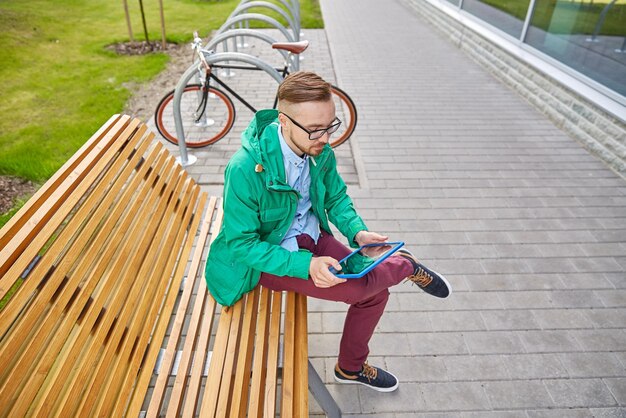 pessoas, estilo, tecnologia e estilo de vida - homem jovem hipster feliz com computador tablet pc e bicicleta fixie sentado no banco na cidade