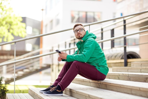 Pessoas, estilo, tecnologia e estilo de vida - jovem hipster com smartphone sentado nas escadas na cidade