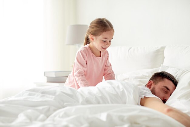 pessoas, família e conceito de manhã - menina feliz acordando seu pai adormecido na cama em casa
