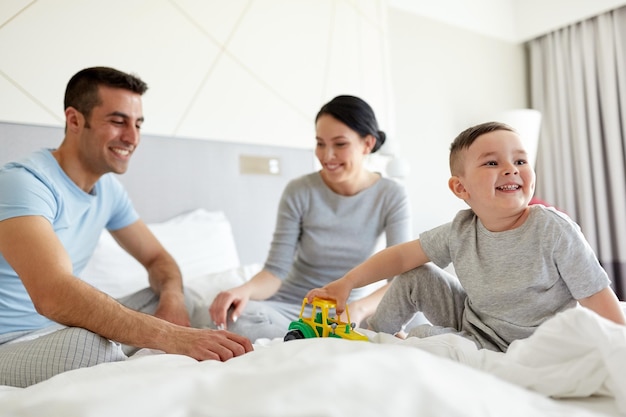 pessoas, família e conceito matinal - criança feliz com trator de brinquedo e pais brincando na cama em casa ou no quarto de hotel