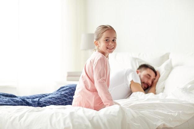 pessoas, família e conceito matinal - menina feliz acordando seu pai dormindo na cama em casa