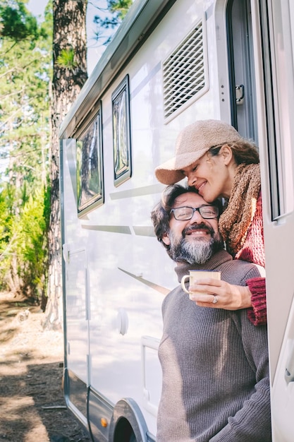 Pessoas felizes em estilo de vida de viagem sentadas na porta de uma caravana estacionando no parque florestal natural desfrutando de uma casa de van, alugando um veículo para férias e uma casa autônoma independente