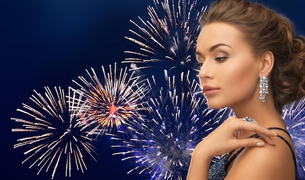 pessoas, feriados e conceito de glamour - linda mulher com brinco de diamante sobre fogos de artifício em fundo azul escuro