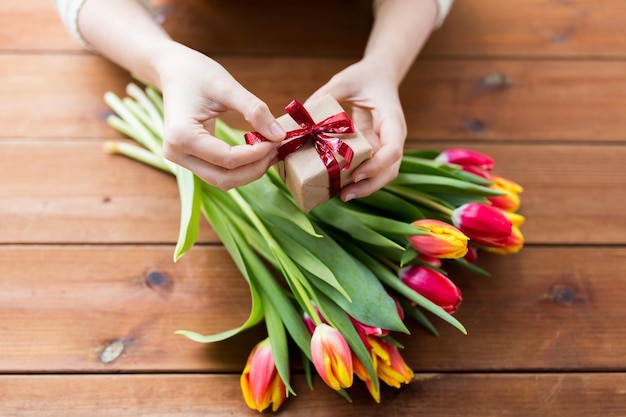 pessoas, feriados e conceito de saudação - close-up da mulher segurando a caixa de presente e flores de tulipa