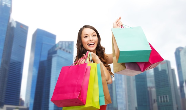 pessoas, feriados, turismo, viagens e conceito de venda - jovem mulher feliz com sacolas de compras sobre fundo de arranha-céus da cidade de singapura