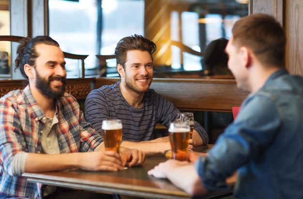 Pessoas, homens, lazer, amizade e conceito de comunicação - amigos do sexo masculino felizes bebendo cerveja no bar ou pub