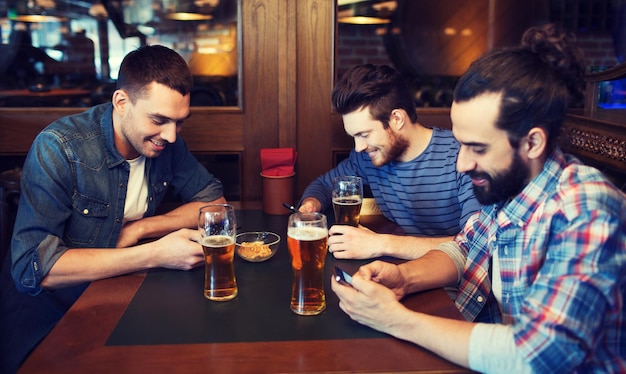 pessoas, homens, lazer, amizade e conceito de tecnologia - amigos do sexo masculino com smartphones bebendo cerveja no bar ou pub