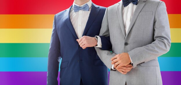 pessoas, homossexualidade, casamento do mesmo sexo e conceito de amor - close-up de casal gay masculino feliz de mãos dadas no casamento sobre fundo de bandeira do arco-íris