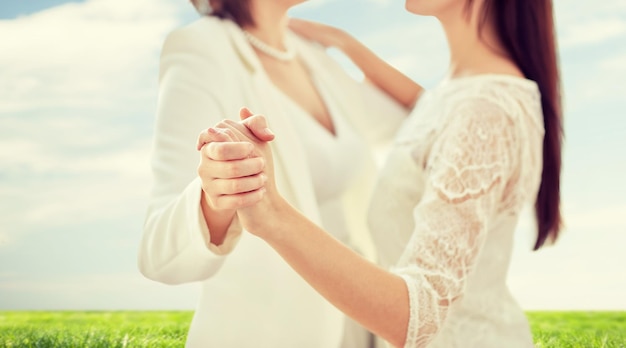 pessoas, homossexualidade, casamento entre pessoas do mesmo sexo e conceito de amor - close-up de feliz casal de lésbicas casados dançando sobre céu azul e fundo de grama