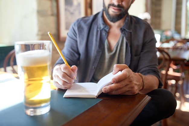 pessoas, inspiração, freelance e conceito de lazer - close-up do homem com cerveja escrevendo para notebook no bar ou pub