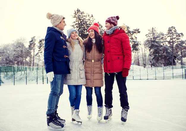 Pessoas, inverno, amizade, esporte e conceito de lazer - amigos felizes patinando no gelo e abraçando na pista ao ar livre